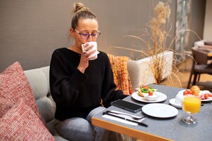 A person sitting at a table with breakfast items, a smartphone, and a glass of orange juice.