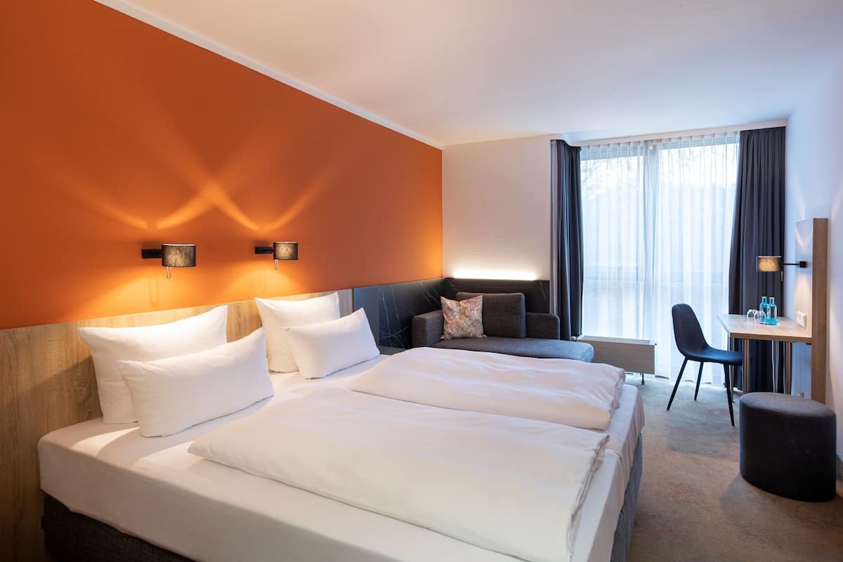A hotel room with two beds, a desk, and a chair.