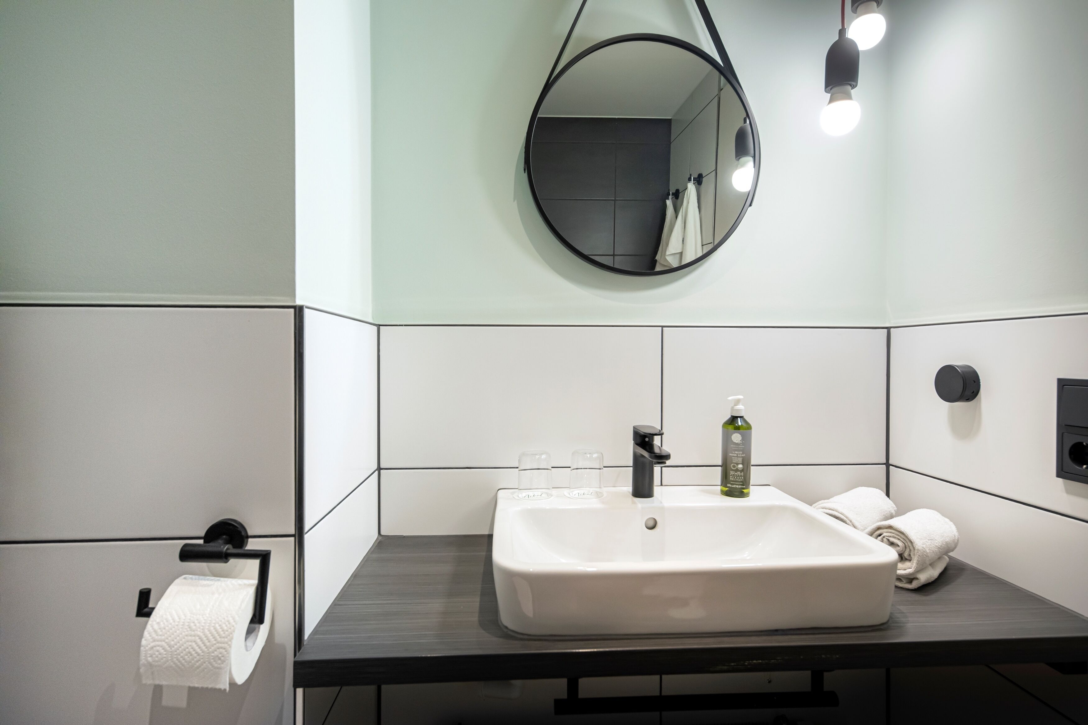 A modern bathroom with a white sink, a round mirror, and a towel rack.