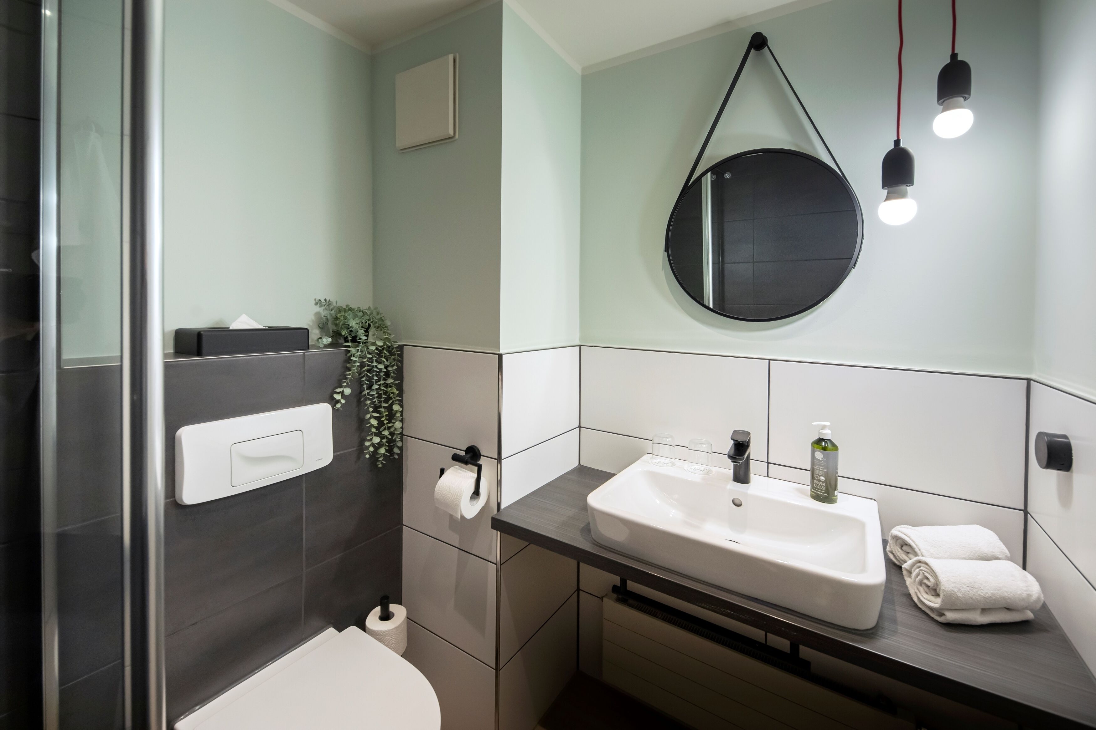 A modern bathroom with a glass shower enclosure, a white sink with a mirror, and a towel rack.