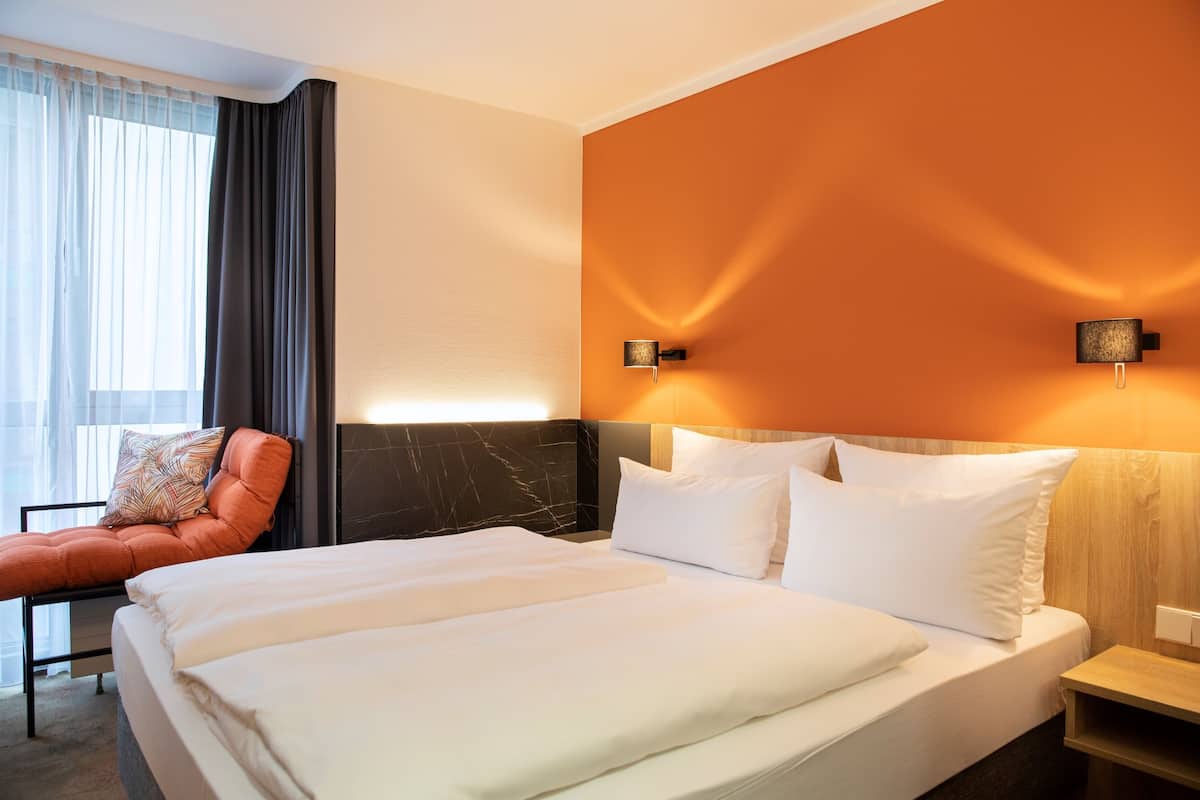 A hotel room with a large bed, two bedside tables, a nightstand, a chair, and a window with curtains.