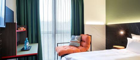 Une chambre d’hôtel avec un lit, une chaise, un bureau avec une bouteille d’eau et un téléviseur posé sur un meuble.