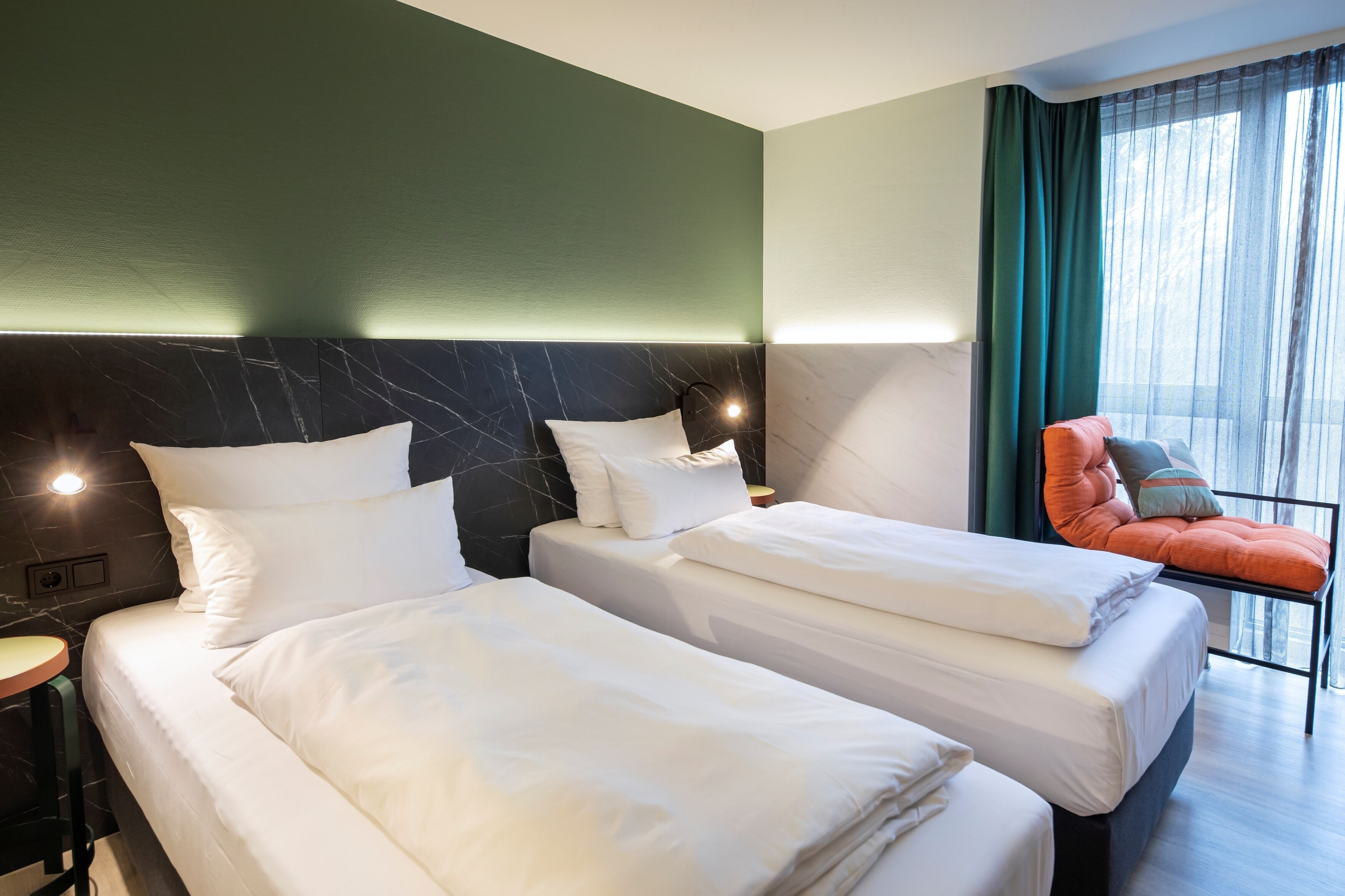 Une chambre d’hôtel avec deux lits, une table de chevet, une chaise et une grande fenêtre avec des rideaux.