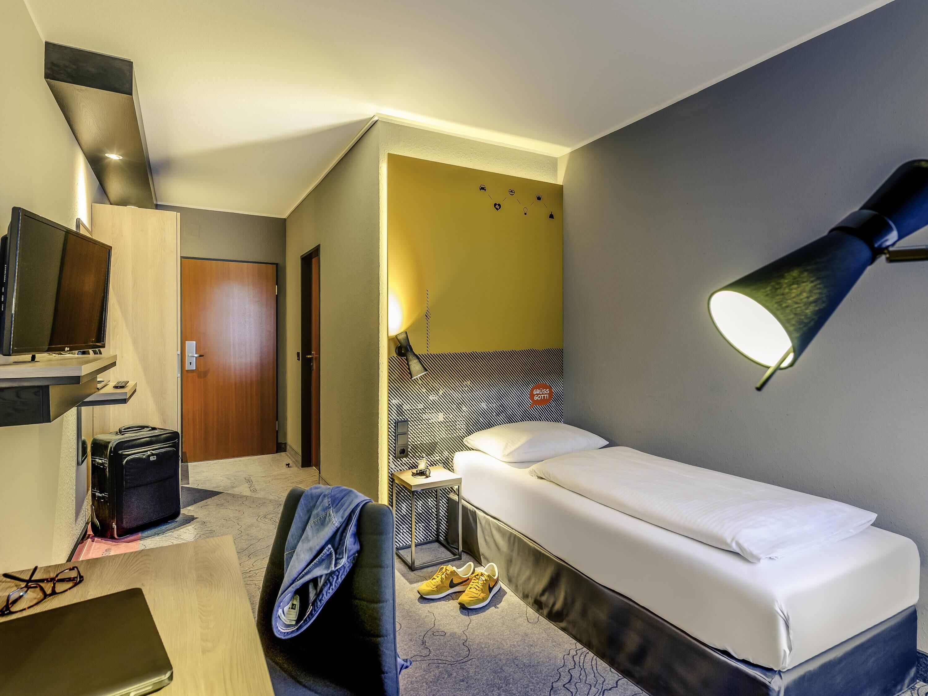 A hotel room with a bed, a desk with a computer, a TV, and a lamp.