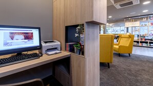 A modern hotel room with a wooden desk, a computer, a printer, and a yellow armchair. - Mercure Hotel Stuttgart Zuffenhausen (Stuttgart)