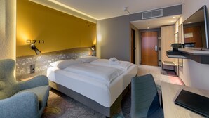 A hotel room with a bed, two chairs, a desk, a mirror, and a wall-mounted phone. - Mercure Hotel Stuttgart Zuffenhausen (Stuttgart)