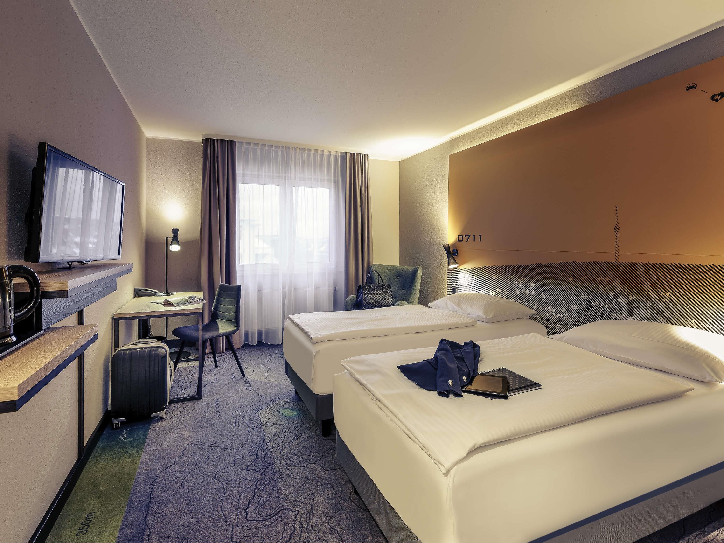A hotel room with two beds, a desk, a chair, a television, and a window with curtains.