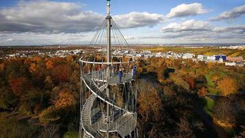 A spiral staircase tower with a viewing platform at the top, surrounded by autumn foliage and a town in the background.