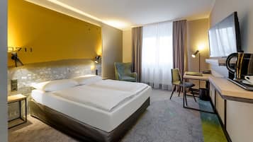 Een hotelkamer met een groot bed, een bureau met stoel, een televisie en een raam met gordijnen.