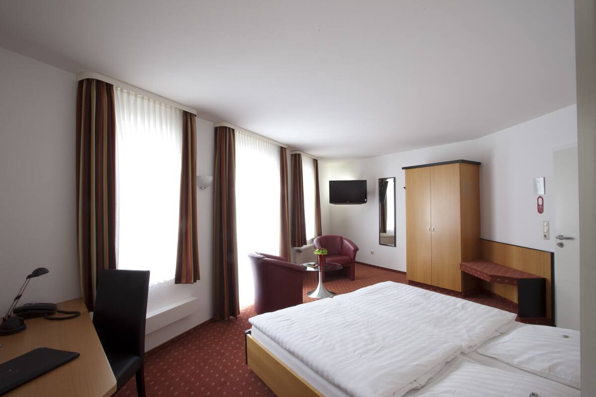Una habitación de hotel con cama, escritorio, silla, televisor y armario.