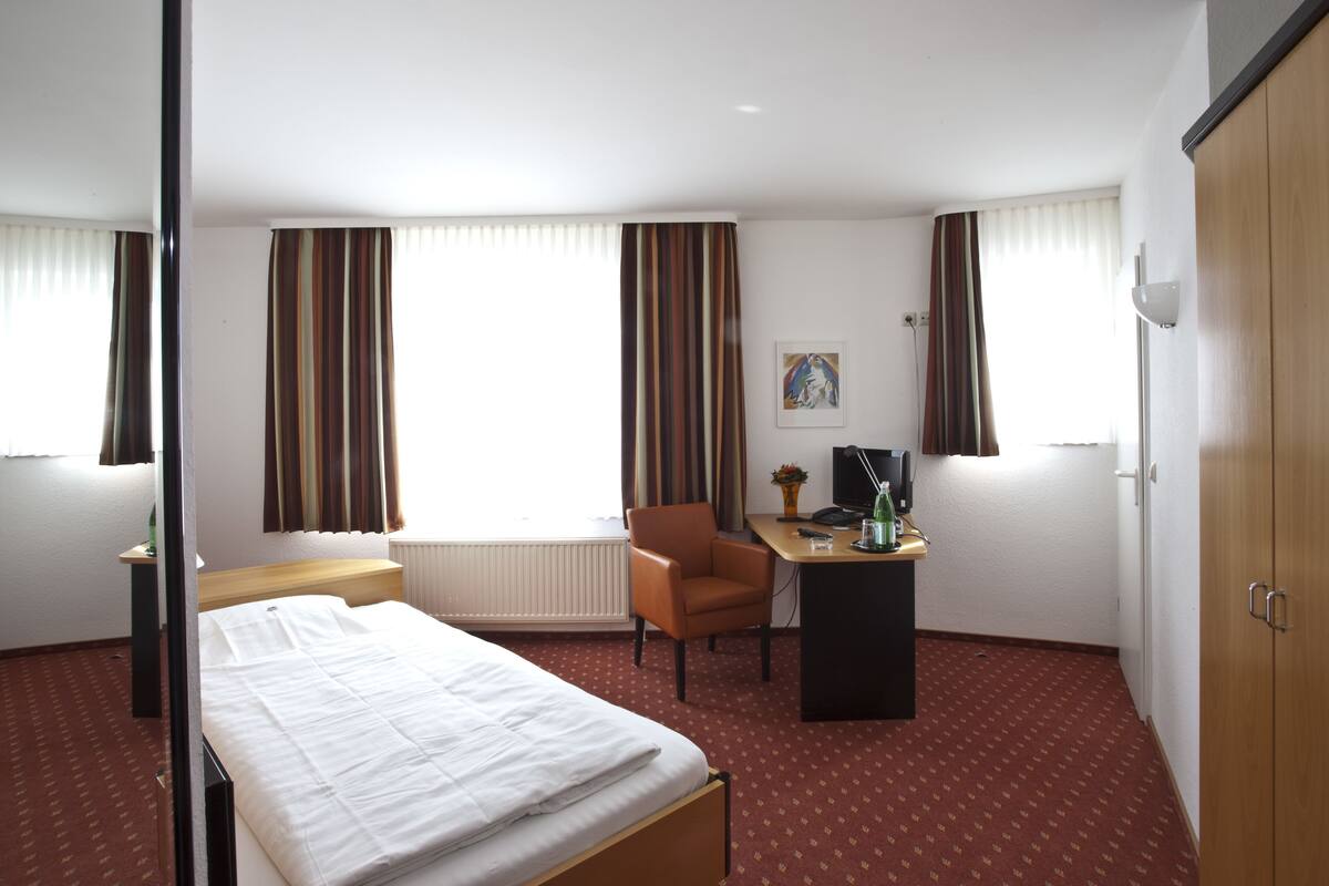 Una habitación de hotel con cama, escritorio, silla, televisor y armario.