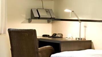 Et hotelværelse med en seng, et skrivebord med telefon, en lampe og et vægmonteret fjernsyn.