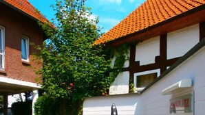 A residential area with a paved driveway, a white wall with a sign, and a red-tiled roof house. - Hotel Am Braunen Hirsch (Celle)