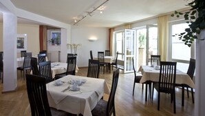 A dining area with multiple tables and chairs, a ceiling with track lighting, and a view of the outdoors through a large window. - Hotel Am Braunen Hirsch (Celle)