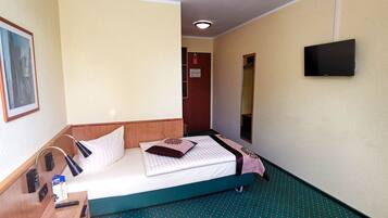Une chambre d’hôtel avec un lit, une table de chevet avec une lampe, un téléviseur fixé au mur et une porte donnant sur une autre pièce.