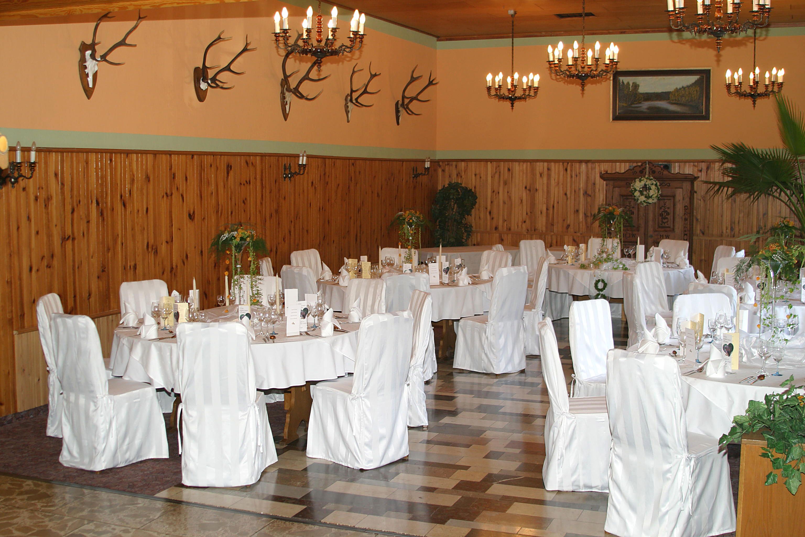A banquet hall with multiple tables set for dining, adorned with white tablecloths and chairs covered in white fabric.