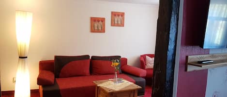 Una sala de estar con un sofá rojo, una pequeña mesita de madera con un jarrón de flores y dos cuadros colgados en la pared.