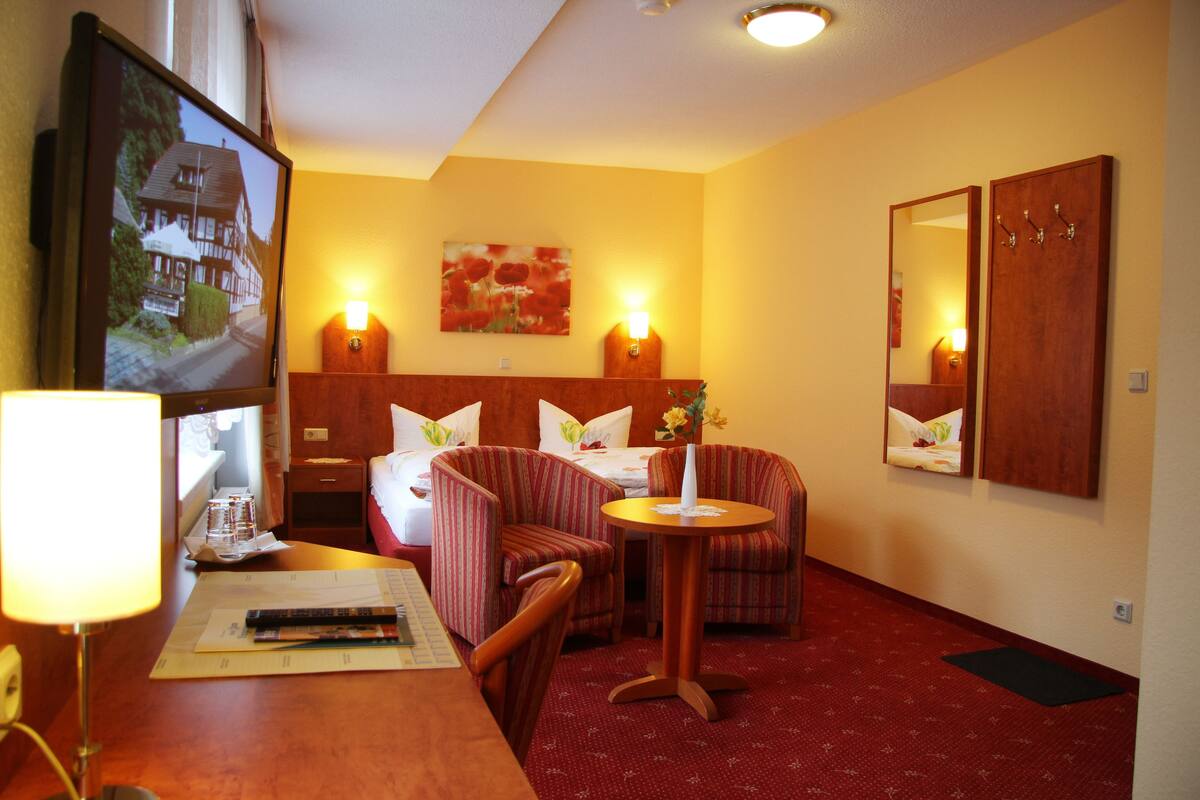 Una habitación de hotel con una cama, dos sillones, una mesita, un televisor y un espejo.