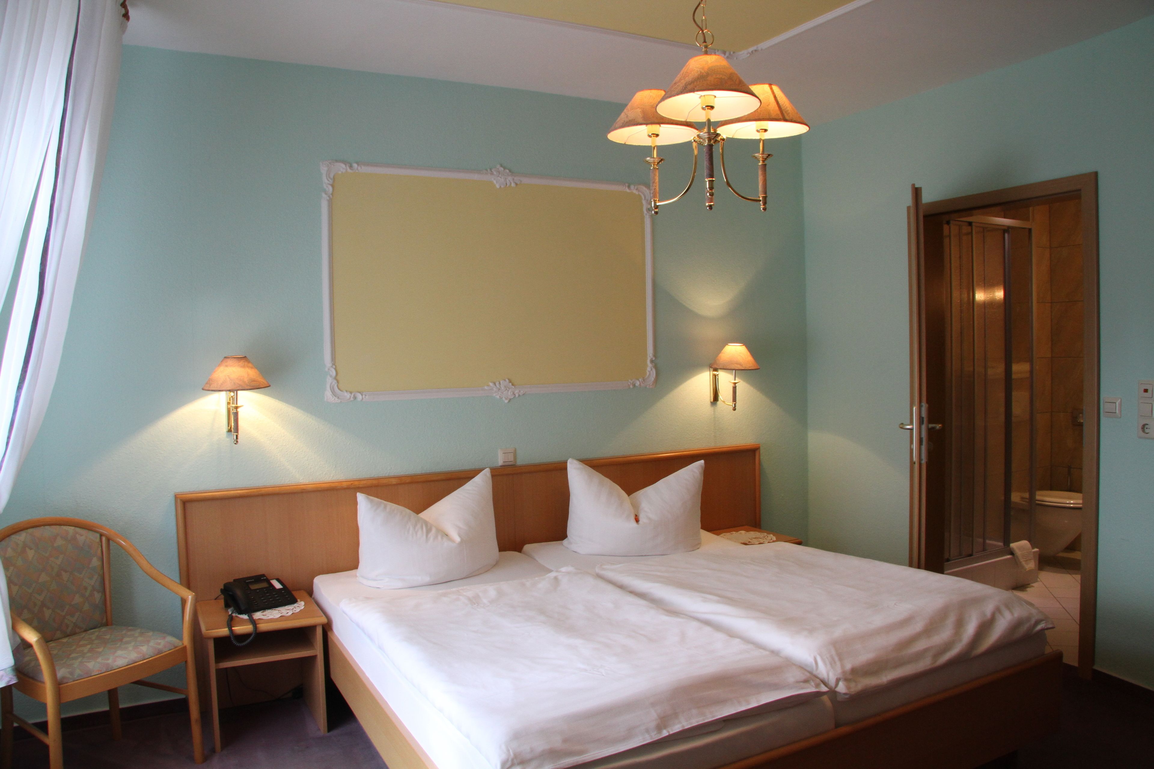 Habitación de hotel con cama, una silla, mesita de noche, lámpara y espejo en la pared.