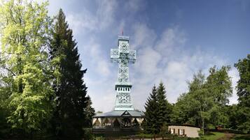 Una torre metálica alta con una cruz en la parte superior, rodeada de árboles y un pequeño edificio en su base.