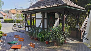 A traditional building with a tiled roof and a covered seating area with benches and potted plants. - Hotel Zum Bürgergarten (Südharz)