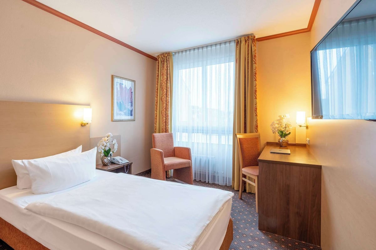 Een hotelkamer met een groot bed, een bureau, een stoel en een raam met gordijnen.