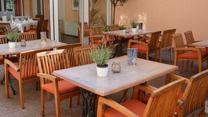 Un espace de restauration en plein air avec des tables et des chaises en bois, des plantes en pot et un présentoir à menus.