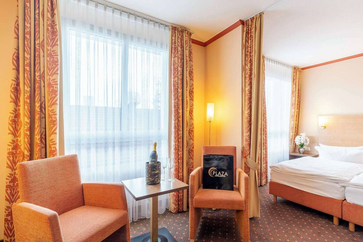 Hotelkamer met een bed, twee fauteuils, een tafeltje met een fles en glazen, en gordijnen met een bloemenprint.