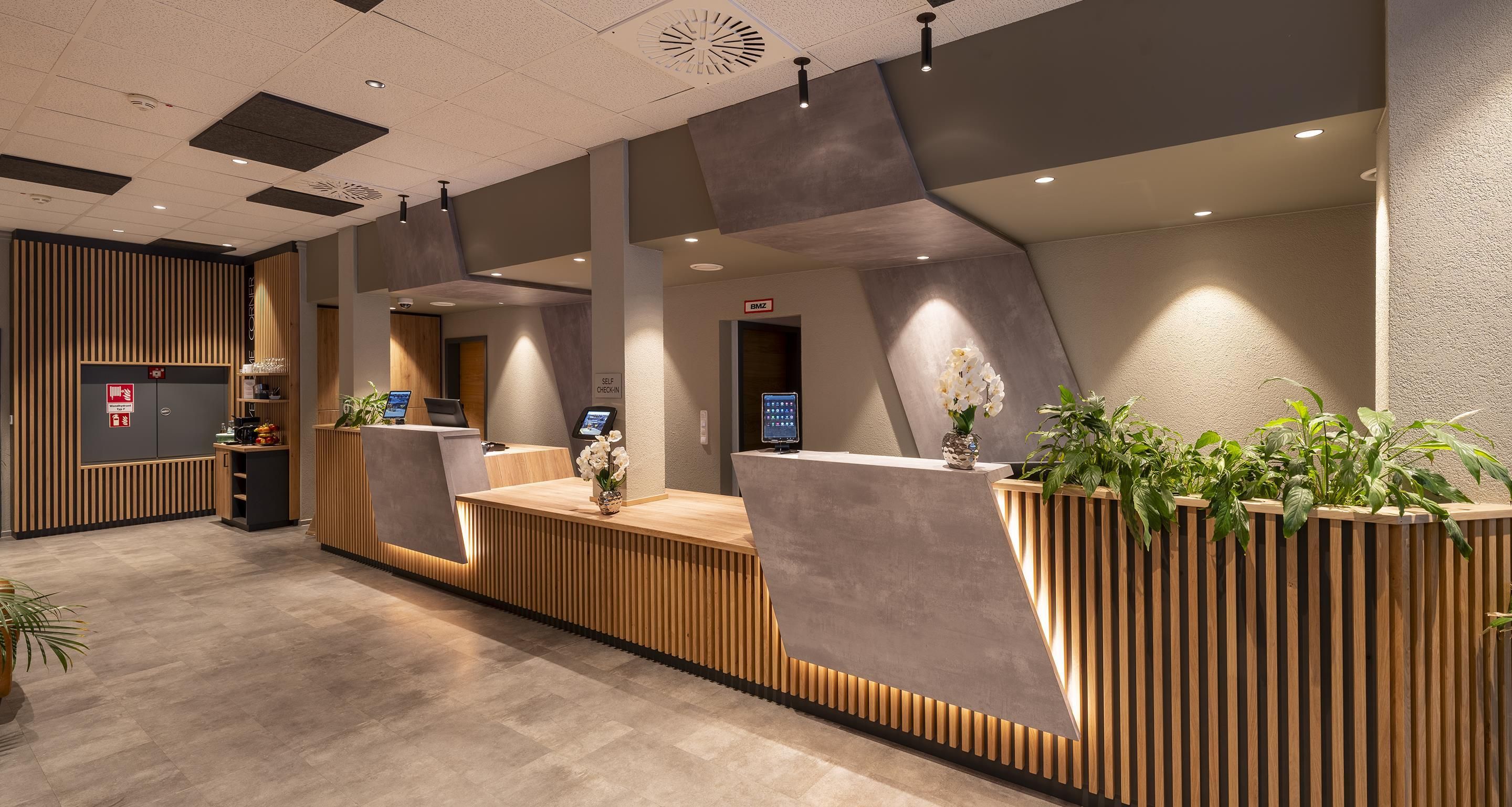 Un'area reception moderna con scrivania in legno, stazione di check-in automatico e chiosco digitale.