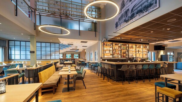 Un ristorante spazioso con soffitti alti, un'area bar centrale e diverse opzioni di posti a sedere, tra cui banconi e tavoli.