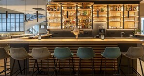 Een bar met een toonbank, barkrukken en schappen vol flessen en glazen.