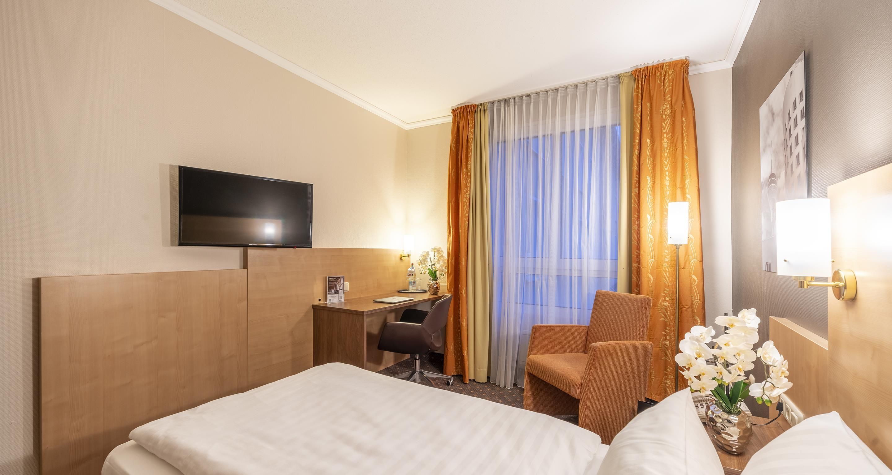 A hotel room with a bed, a desk, a chair, a television, and a window with curtains.