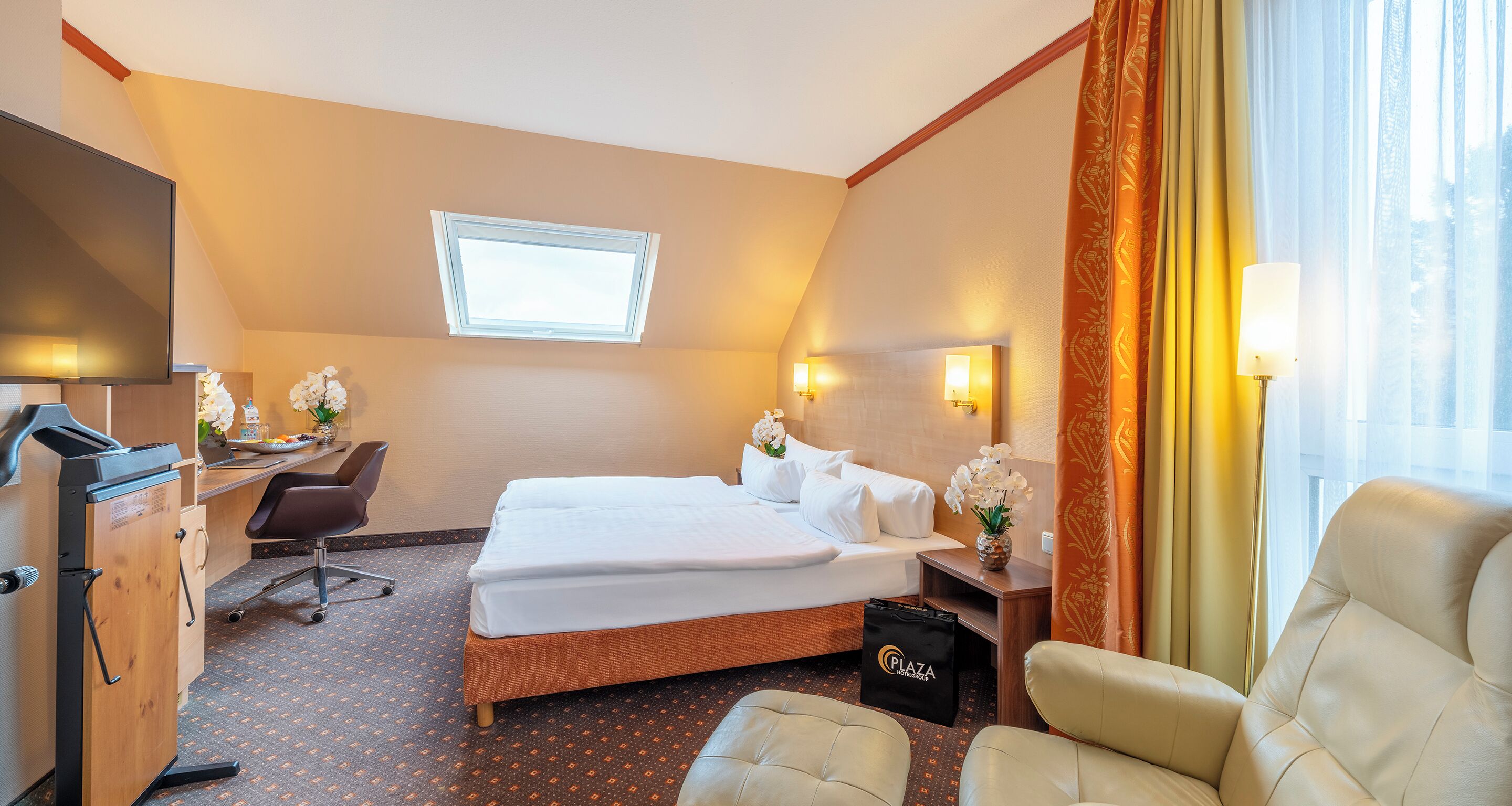 Une chambre d’hôtel avec un lit, un bureau, une chaise et une petite table sur laquelle est posé un vase de fleurs.