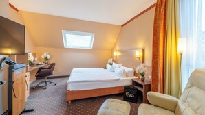 Une chambre d’hôtel avec un lit, un bureau, une chaise et une petite table sur laquelle est posé un vase de fleurs.
