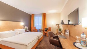 Camera d'albergo con un letto grande, una scrivania con un portatile, una sedia, una televisione e un minibar.