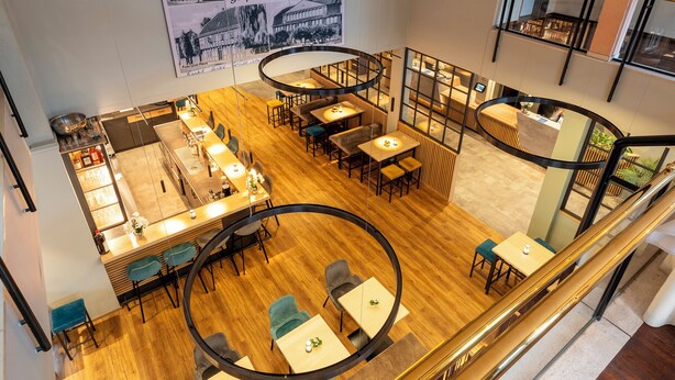 Un restaurant moderne doté d’un bar central, de plusieurs espaces de restauration et offrant une vue sur le paysage urbain.