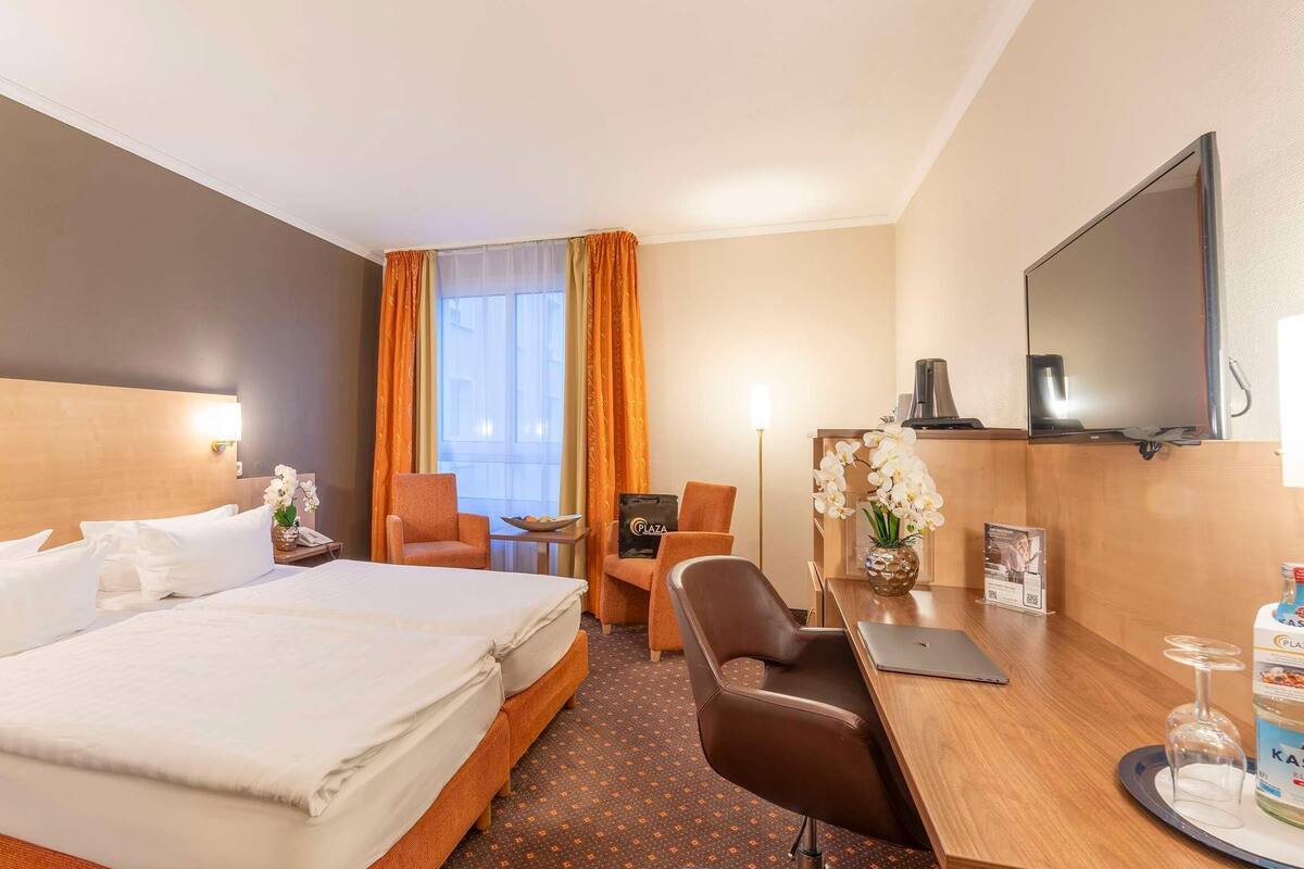 Een hotelkamer met een groot bed, een bureau met een laptop, een stoel, een televisie en een minibar.
