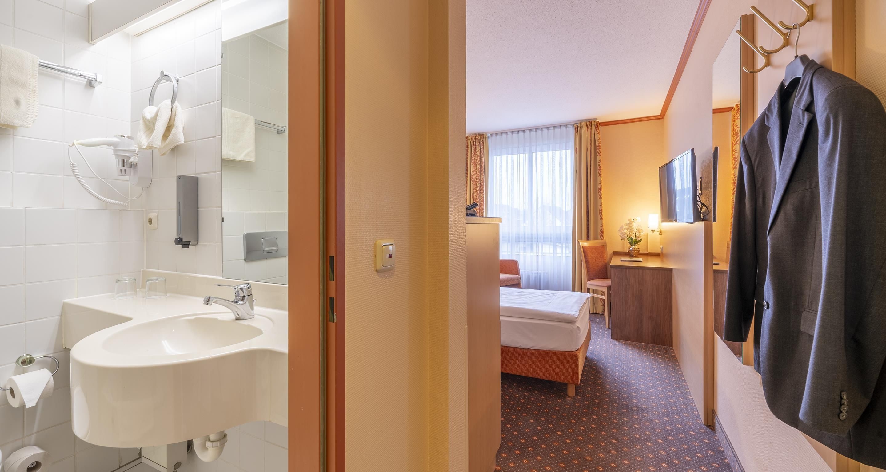Een hotelkamer met een badkamer, een bed, een bureau en een kapstok.