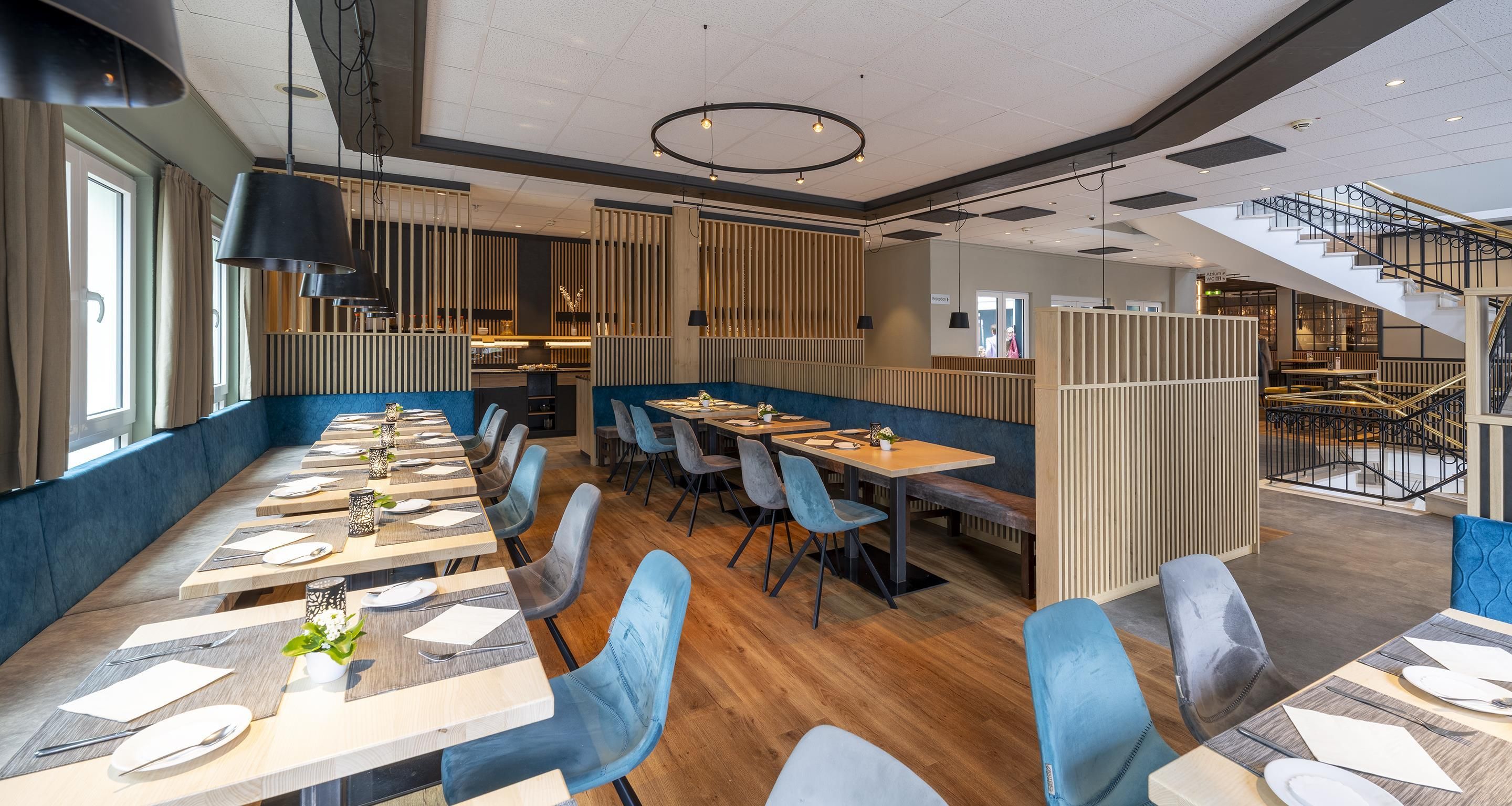 Un restaurant moderne avec une longue table à manger, des chaises à revêtement bleu et un plancher en bois.