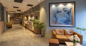 Een hotel lobby met een receptiebalie, een groot abstract schilderij, een leren bank en een kamerplant.