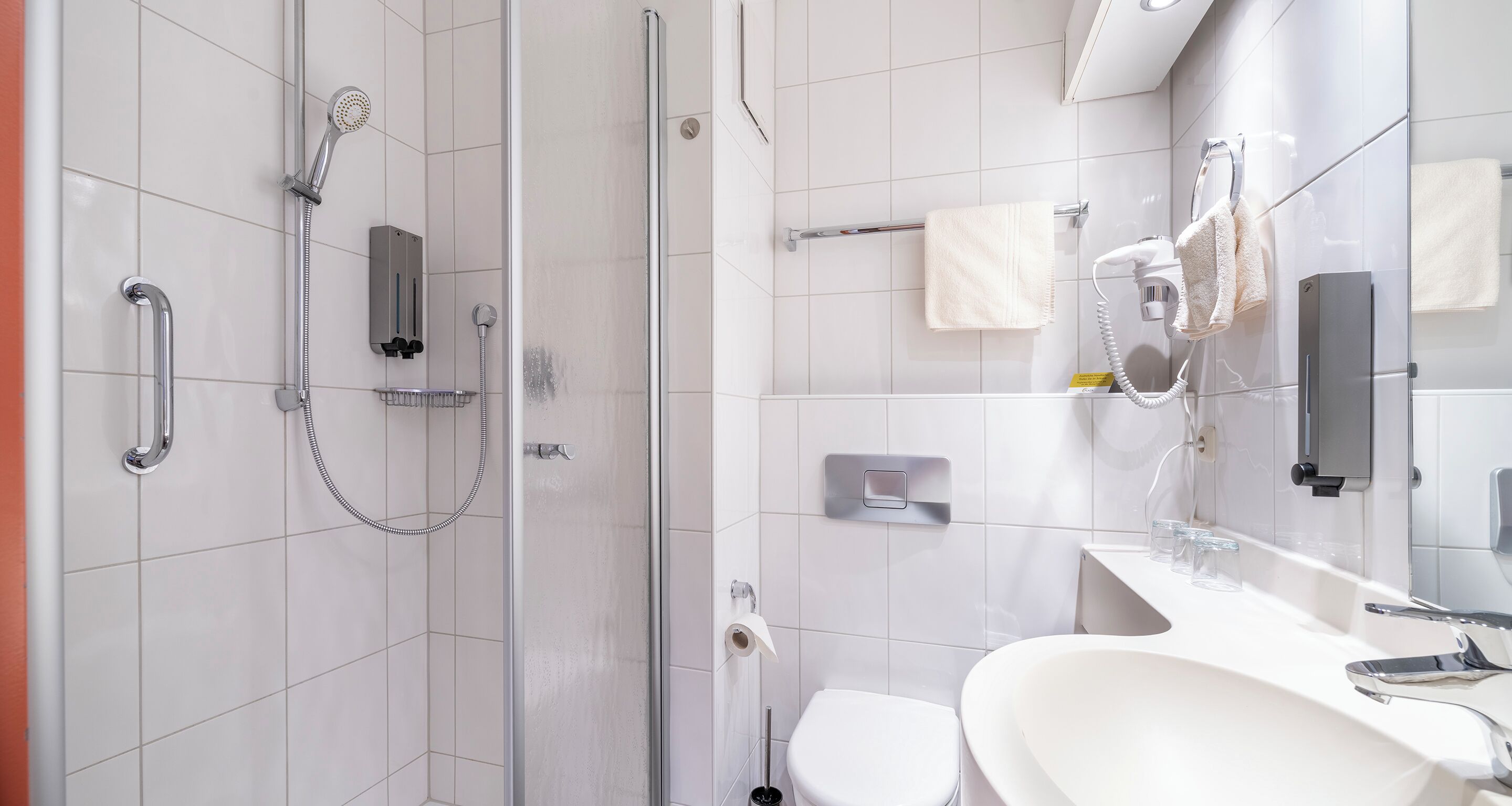 Uma casa de banho moderna com cabine de duche em vidro, lavatório branco e espelho.