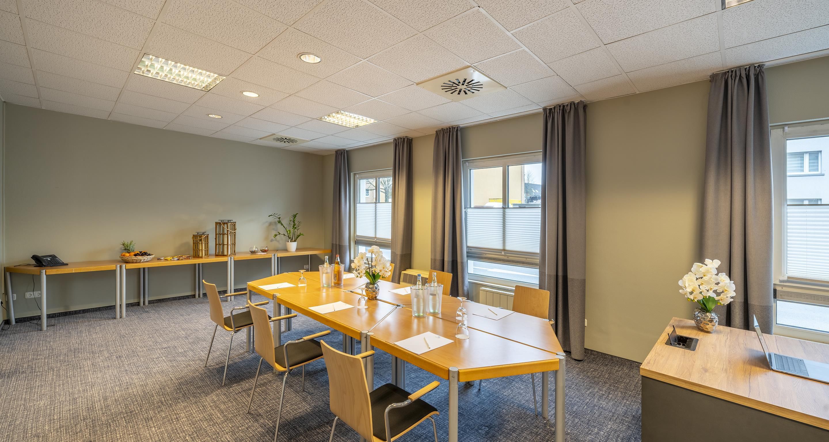 Et mødelokale med et langt bord, stole, en lille reception og et vindue med gardiner.