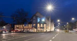 Een hotel met een modern ontwerp, gelegen bij een straatovergang met duidelijke wegmarkeringen en verkeerslichten.