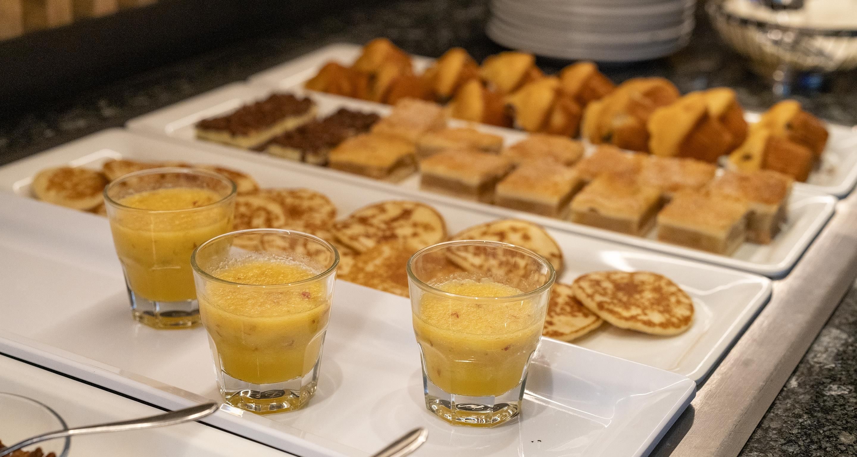 A breakfast buffet with various pastries and a glass of orange juice.