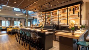 Zona bar moderna con un bancone in legno, sgabelli da bar e diverse bottiglie e bicchieri su mensole.