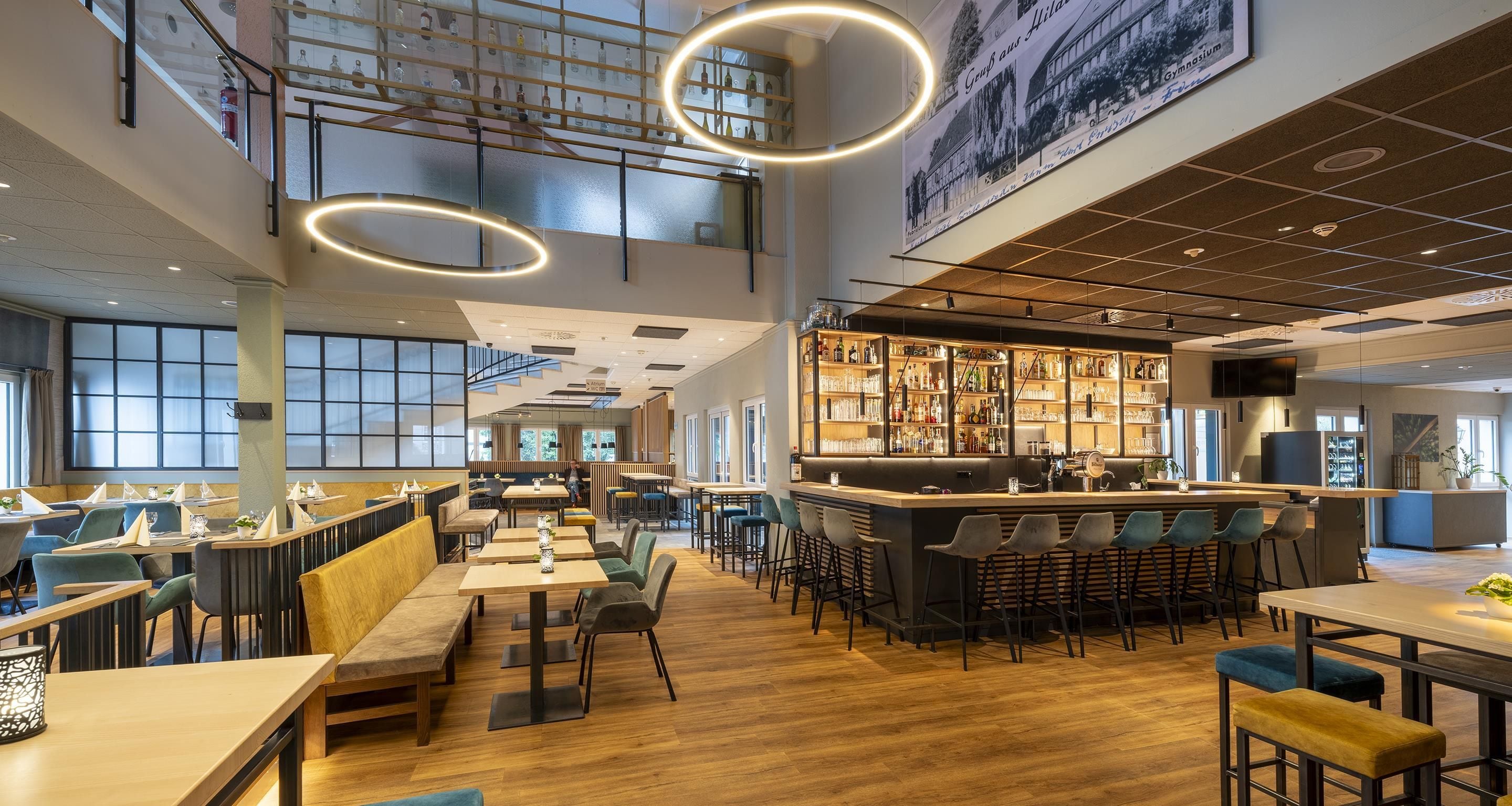 A spacious restaurant with high ceilings, a bar area, and a view of the cityscape through large windows.