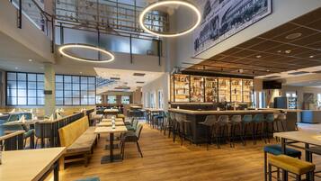A spacious restaurant with high ceilings, a bar area, and a view of the cityscape through large windows.