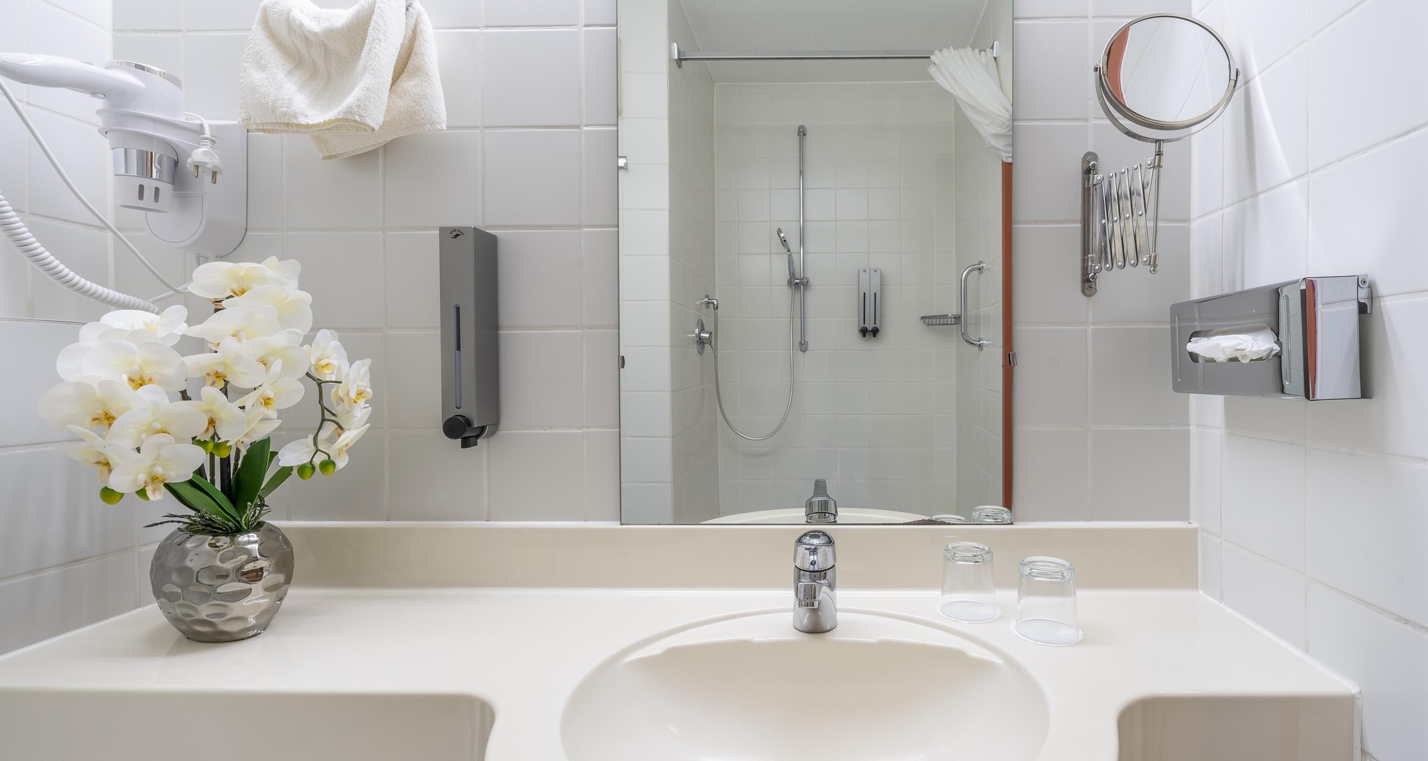 Un baño con lavamanos blanco, ducha de mano, toallero, espejo y teléfono.