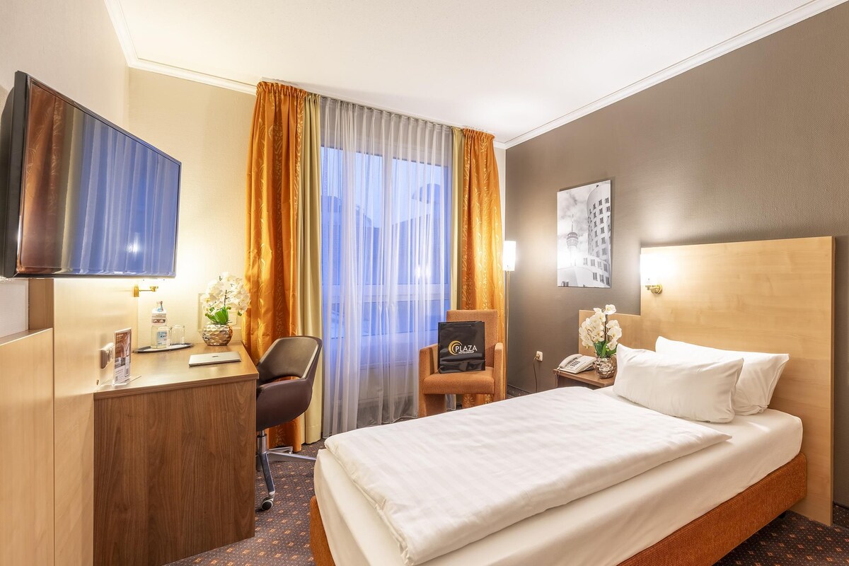 A hotel room with a bed, a desk, a chair, a television, and a nightstand.