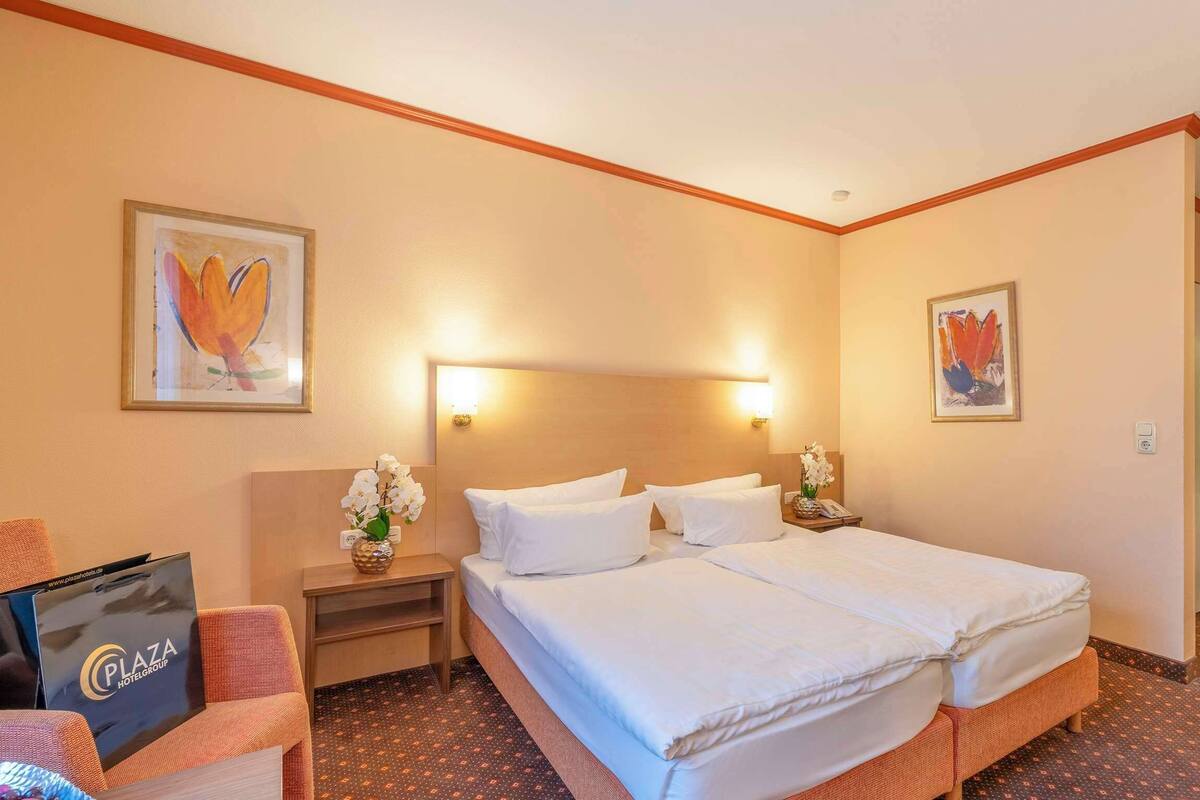 Hotelkamer met een tweepersoonsbed, twee nachtkastjes, een stoel en een bureau met een computer.